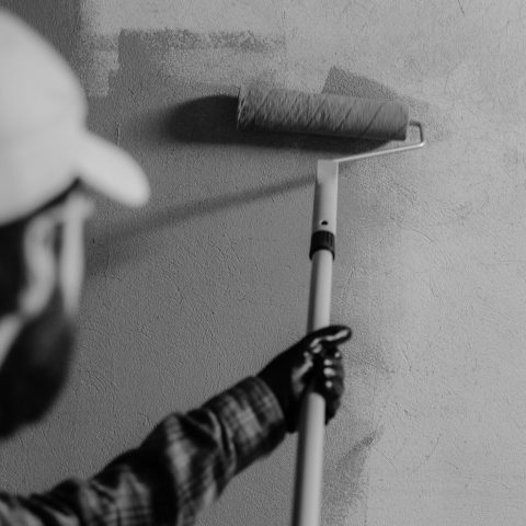 Black and white image of a painter using a roller on an interior wall.